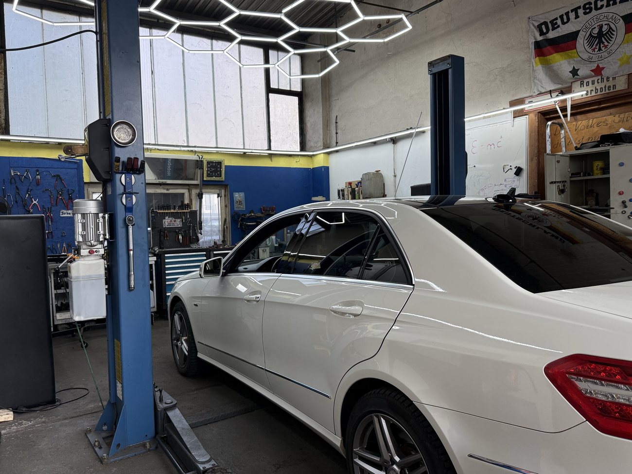 Fahrzeug auf der Hebebühne unter einer sechseckigen LED-Lichtinstallation in der Werkstatt